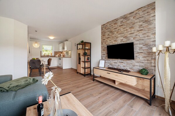Un salon moderne doté d’un téléviseur à écran plat, d’une console en bois et d’un coin repas avec une cuisine en arrière-plan.