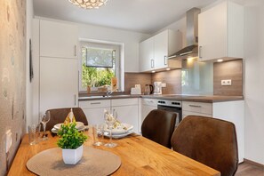 Une cuisine moderne avec des meubles blancs, une table à manger en bois et une vue sur la verdure à l’extérieur.