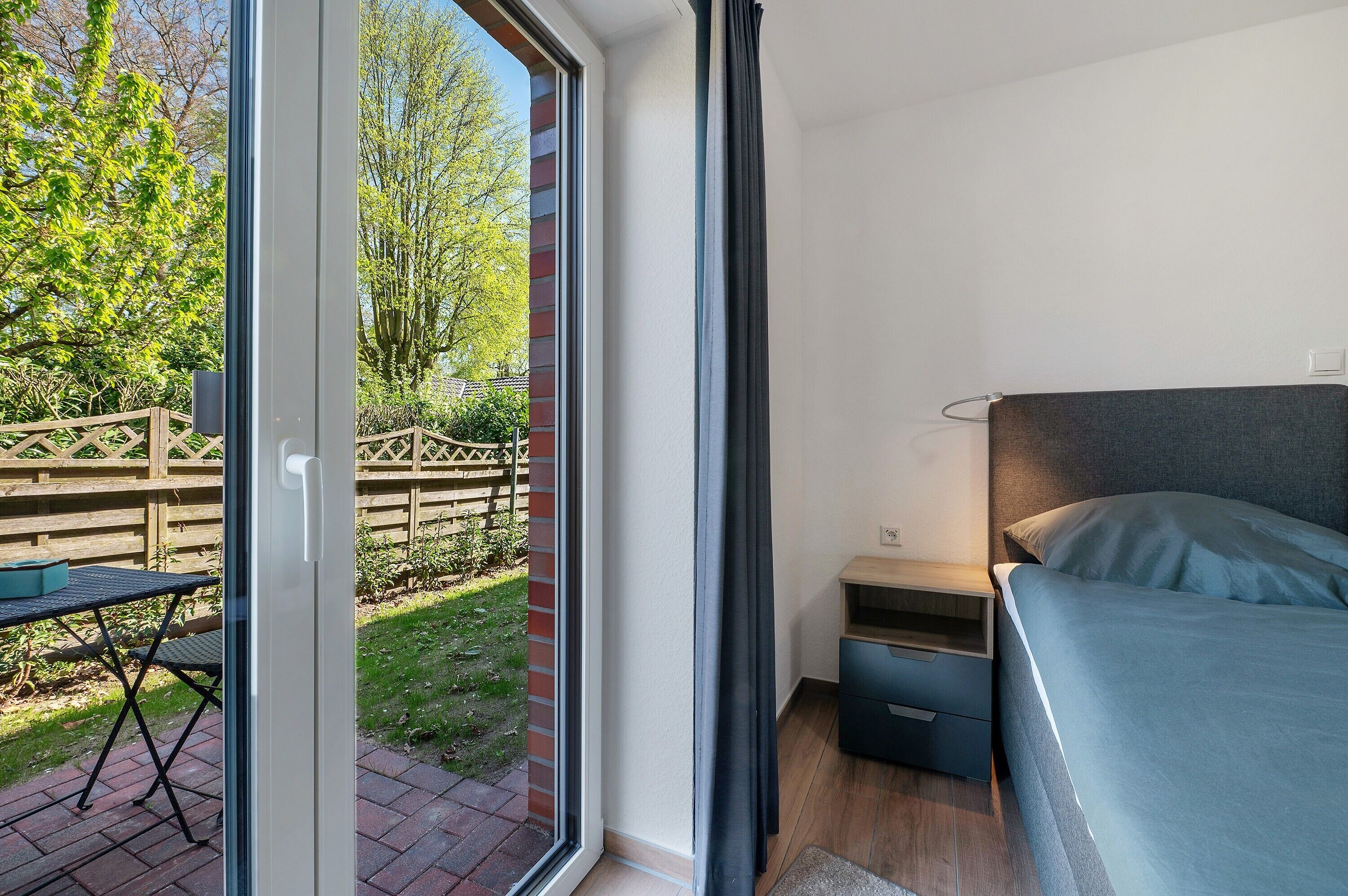 Une chambre à coucher avec un lit, une table de chevet, une fenêtre avec des rideaux et une vue sur un jardin.