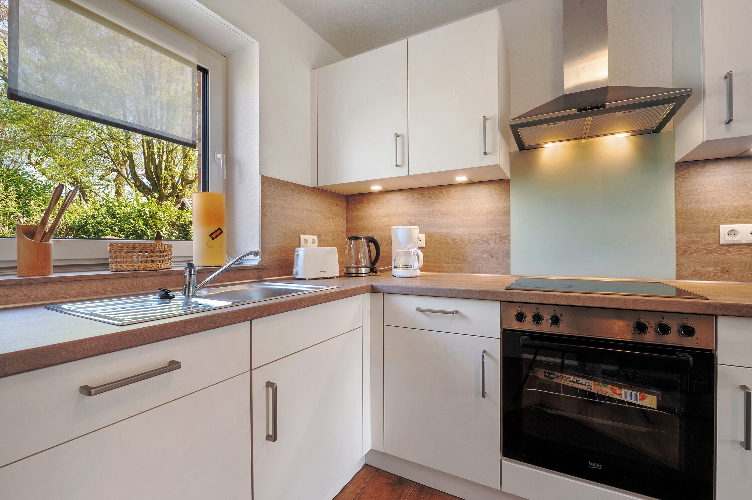 A modern kitchen with white cabinets, a stainless steel oven, and a window with a view of greenery.