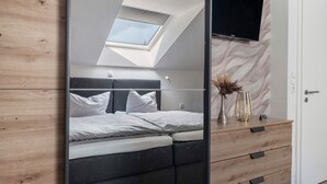 Ein Schlafzimmer mit Dachfenster, einem Bett, einem Schminktisch und einem Fernseher an der Wand.