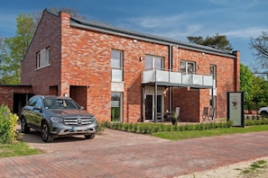 A brick building with a car parked in front, a covered outdoor seating area, and a signboard. - Holiday Apartment 'Anna 1 Og' with Balcony (Suhle)