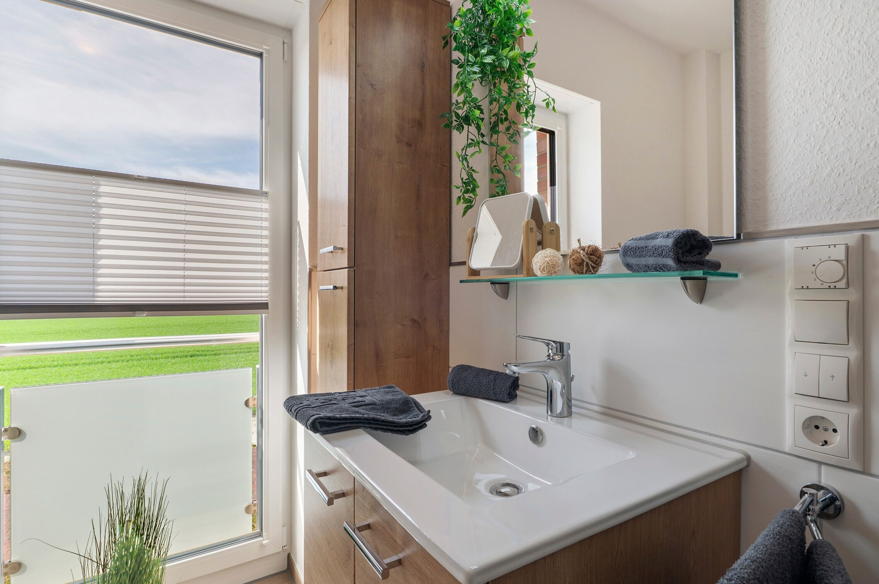 A bathroom with a large window, a sink, a mirror, and a shelf with toiletries.