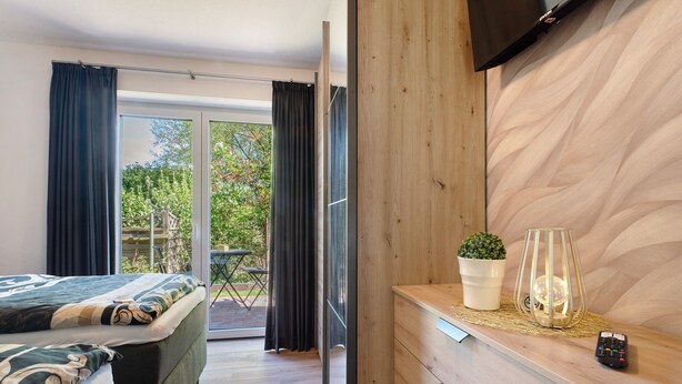 A bedroom with a bed, a TV, a wooden dresser, a plant, and a remote control. - Holiday Apartment 'Anna 2 Eg' with Private Terrace and Garden (Suhle)