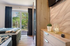 Un dormitorio con una cama, televisor, cómoda de madera, una planta y un control remoto.