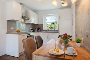 Una cocina moderna con armarios blancos, una mesa de comedor con sillas y un ventanal con vistas a zonas verdes.
