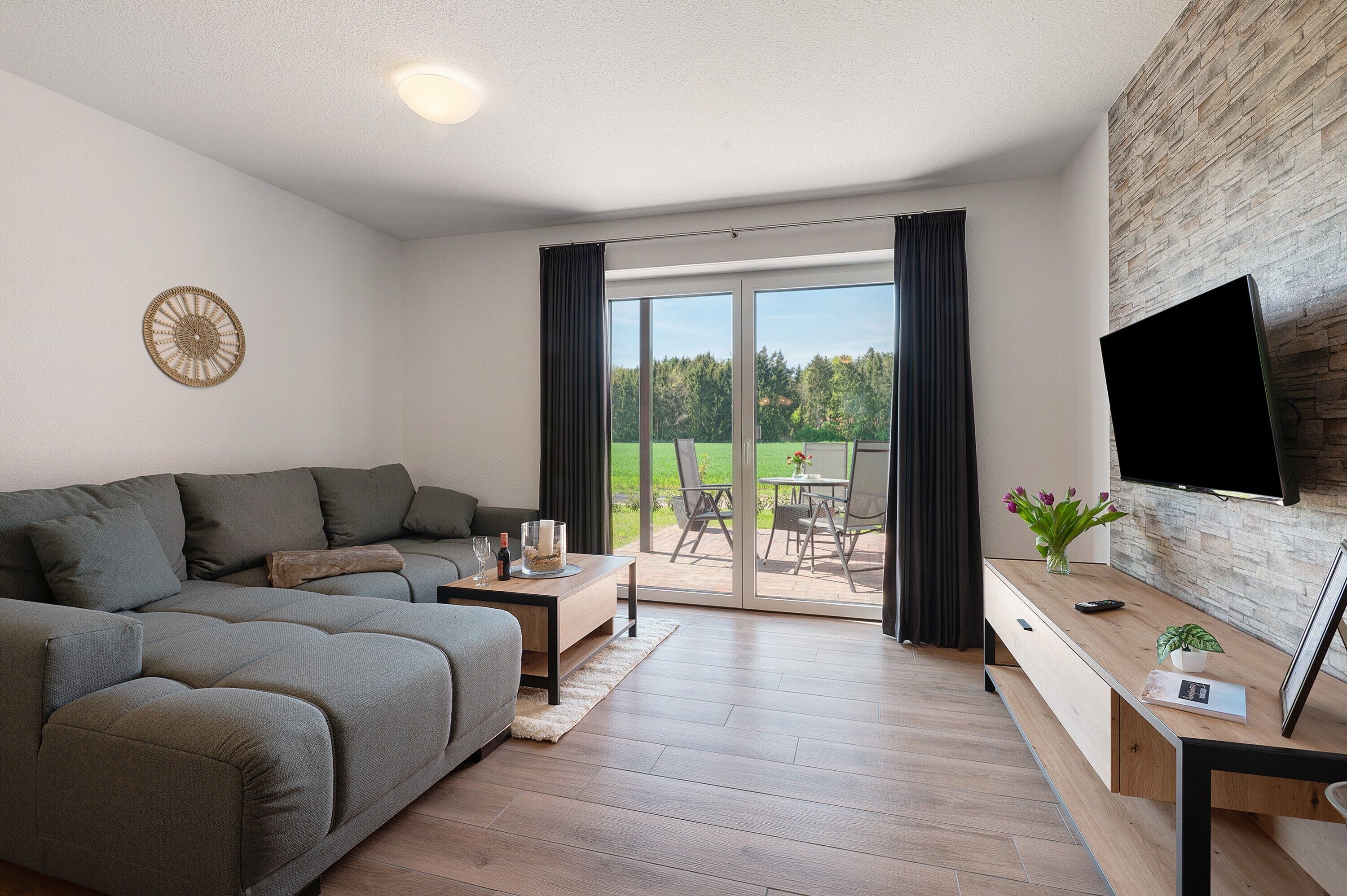 A modern living room with a sectional sofa, a flat-screen TV, a wooden coffee table, and a sliding glass door leading to an outdoor patio.