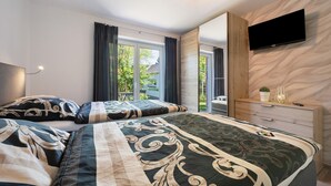 A bedroom with two beds, a TV mounted on the wall, a wooden dresser, and a window with curtains. - Holiday Apartment 'Anna 2 Eg' with Private Terrace and Garden (Suhle)