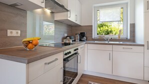 A modern kitchen with white cabinets, a wooden countertop, a stove, and a window with a view of greenery. - Holiday Apartment 'Anna 2 Eg' with Private Terrace and Garden (Suhle)