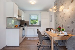 Una cocina moderna con armarios blancos, una mesa de comedor de madera y una ventana con vistas a zonas verdes.