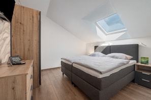 Et soveværelse med ovenlys, en seng, et natbord og en trækommode.