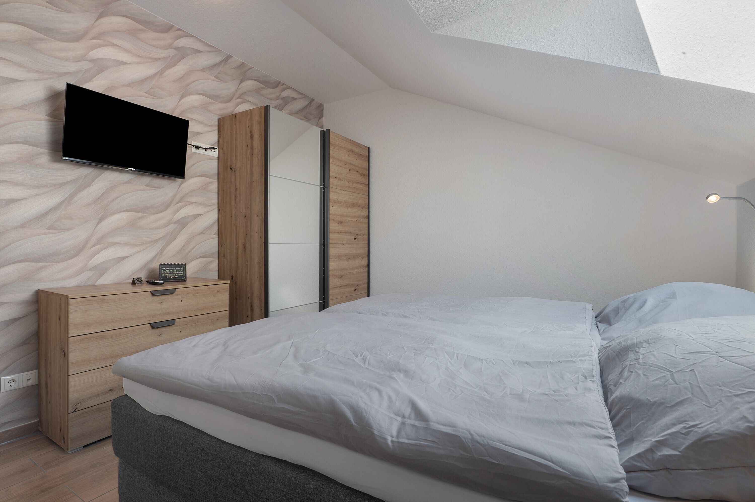 A bedroom with a bed, a dresser, a TV mounted on the wall, and a mirror.
