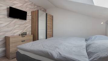 A bedroom with a bed, a dresser, a TV mounted on the wall, and a mirror.