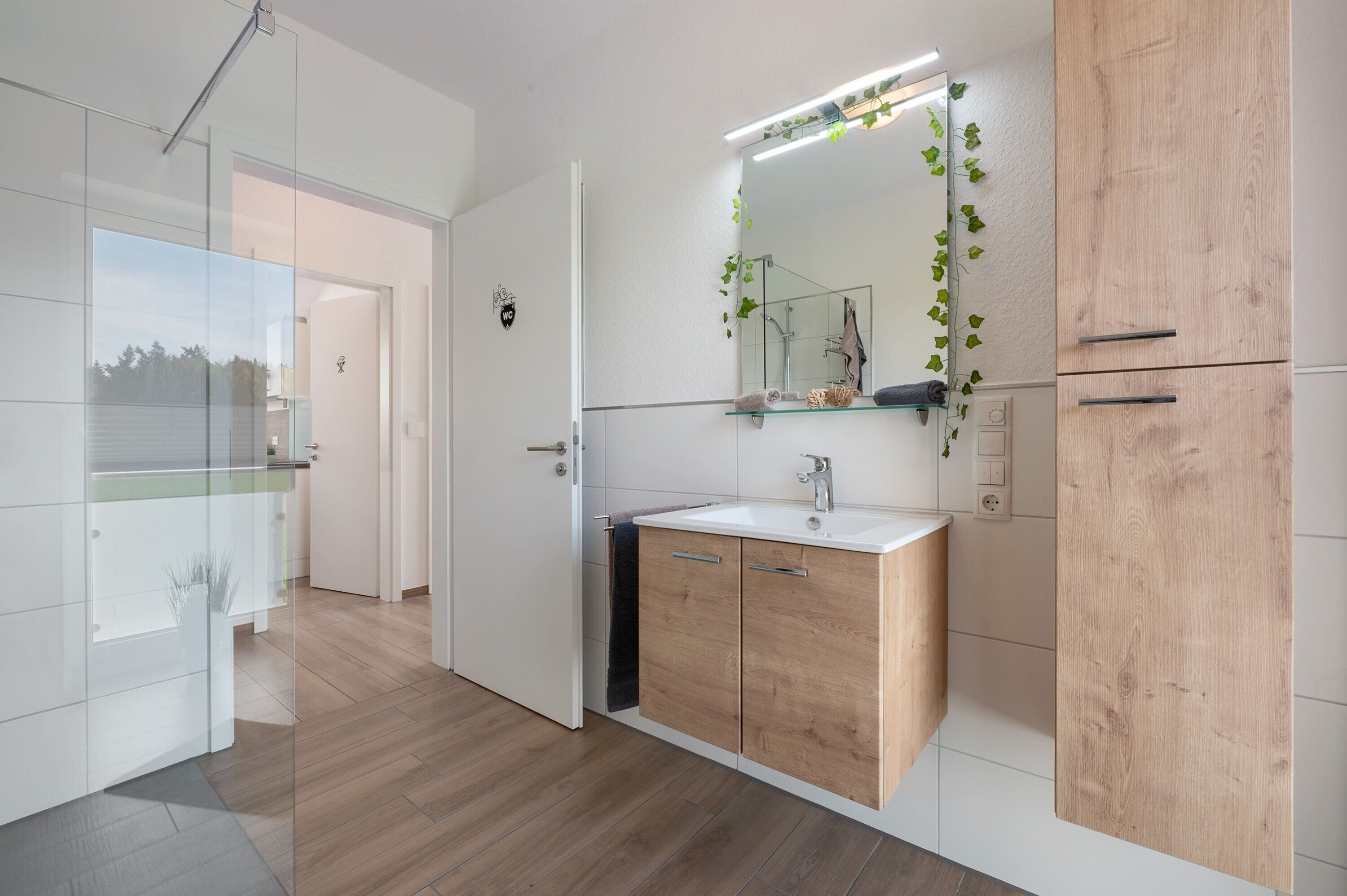 A modern bathroom with a glass shower enclosure, a wooden vanity, and a mirror with a light above it.