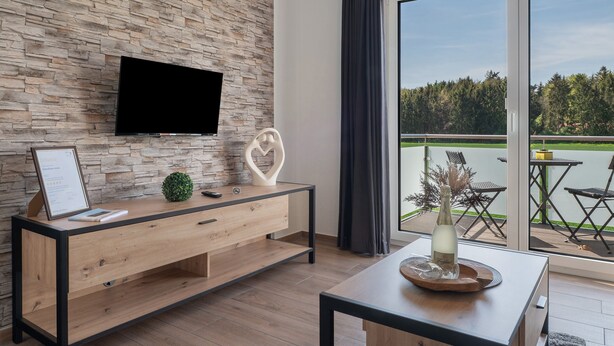 A modern room with a stone wall, a flat-screen TV, a wooden console table, and a balcony with outdoor furniture. - Holiday Apartment 'Anna 2 Og' with Balcony (Suhle)