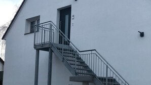 Ein Gebäude mit einer Treppe, die zu einer Tür führt, einem kleinen Fenster und einem Metallgeländer.