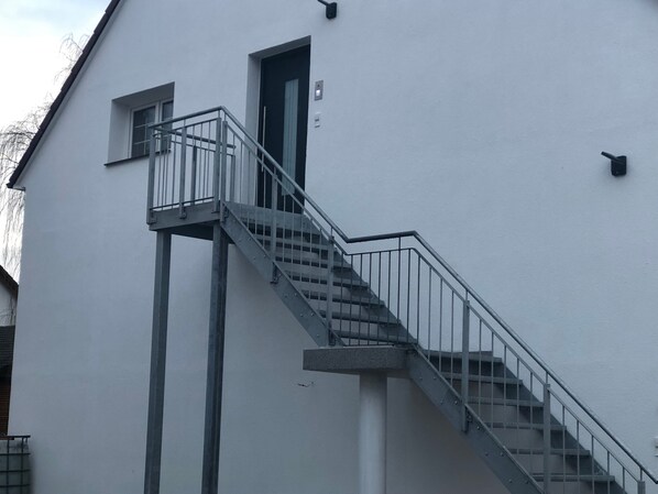 A building with a staircase leading to a door, a small window, and a metal railing.