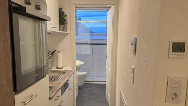Ein schmaler Flur mit einer Küchenzeile an einer Seite, einer Toilette und einem Fenster zum Außenbalkon.