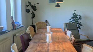 A dining room with a wooden table, white chairs, and a hanging light fixture. - Vacation apartment in a cozy farmhouse by the bathing lake with large garden and sauna (Carpin)