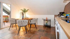 A modern kitchen with a dining area, featuring a round table, cushioned chairs, and a potted plant.