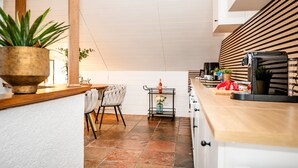 A modern kitchen with a wooden countertop, a dining area with a chair, and a small table with a vase and a bottle.