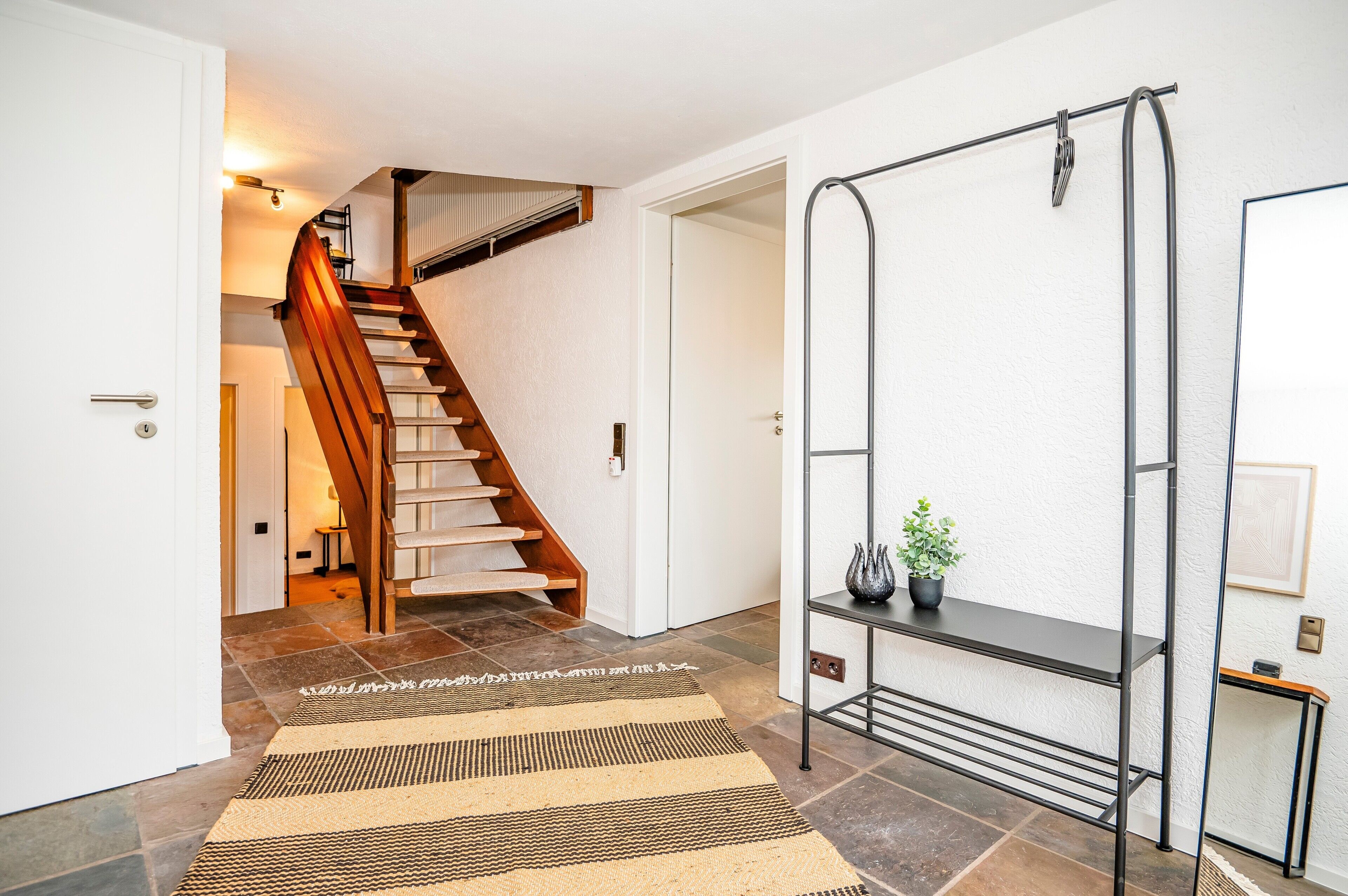 En trappe op til en etage, en metalkasse med en plante, og en dør med lyskontakt.