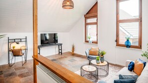A modern loft-style living area with a wooden ceiling, a TV, a sofa, a coffee table, and a dining table.