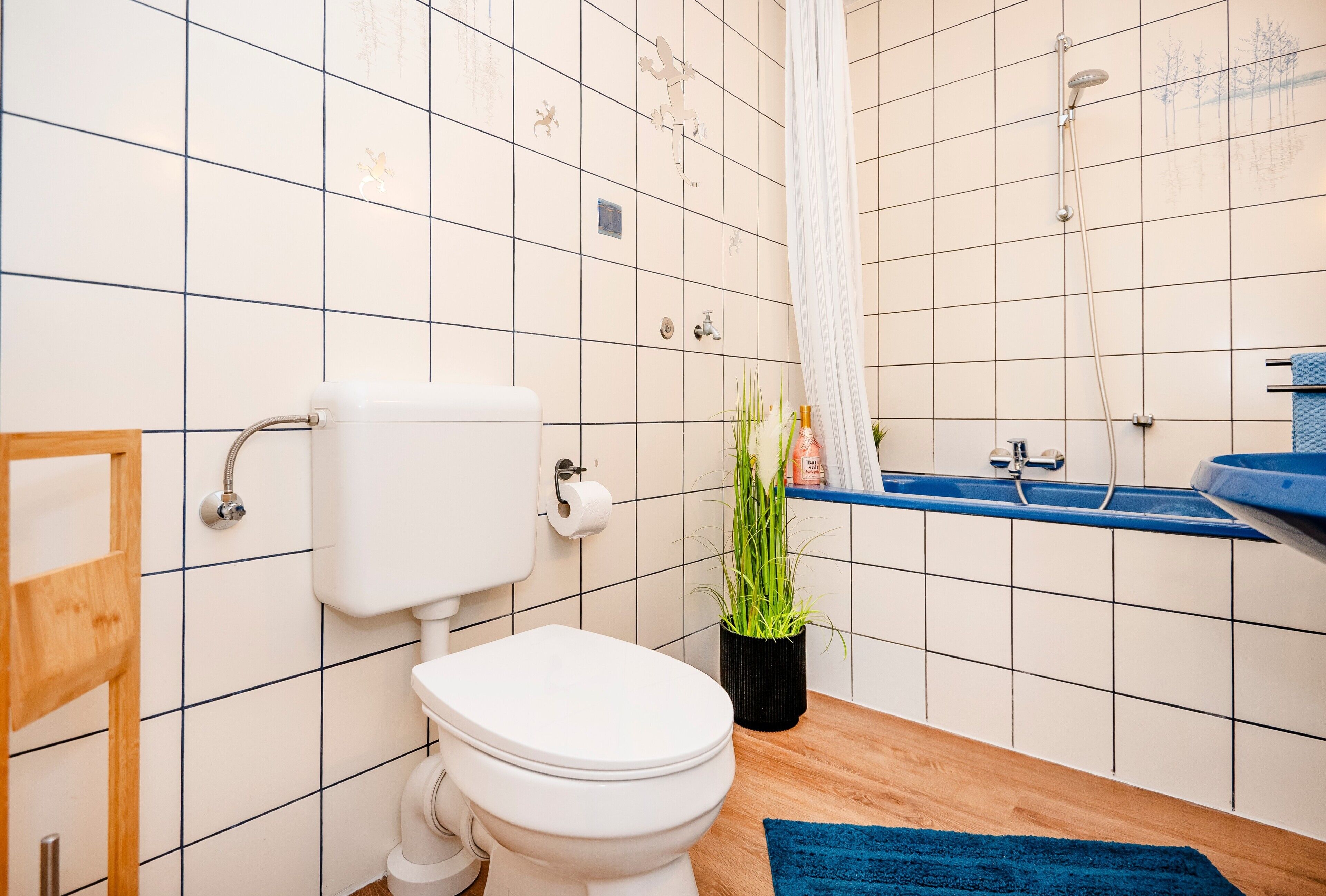 A bathroom with a toilet, shower, sink, and a blue rug.
