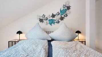 Un dormitorio con cama, almohadones a rayas, un cuadro de peces y dos lámparas de noche.