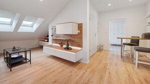 A modern loft apartment with a high ceiling, skylights, a built-in kitchen counter, and a dining area.