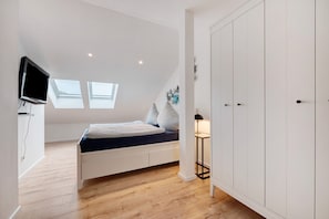 Un dormitorio con cama, televisor, armario y dos tragaluces.