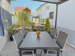 A patio with a table and chairs, surrounded by plants and a stone wall.