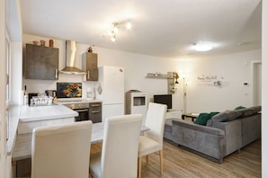 A modern kitchen with a dining area, a grey sofa, and a flat-screen TV. - Apartment 'Auszeit Im Tal Der Liebe' with Private Terrace, Private Garden and Wi-Fi (Deggenhausertal)