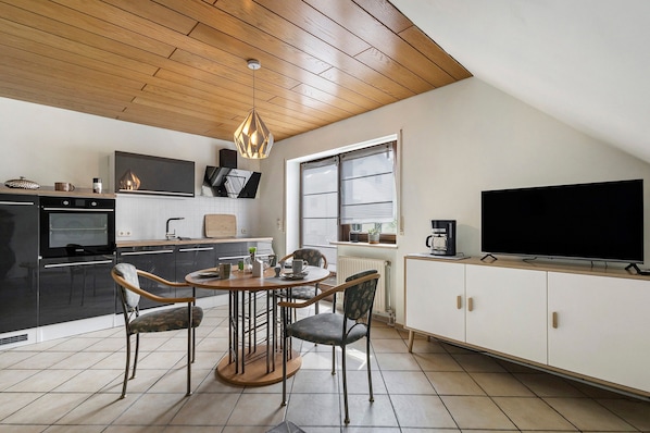 Eine moderne Küche mit Essbereich, Holzboden und einem großen Fernseher.
