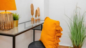 Una habitación moderna con una mesa de vidrio, una lámpara amarilla, una silla con cojín amarillo y detalles decorativos de madera.