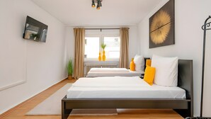 Un dormitorio moderno con cama, mesitas de noche, televisor de pantalla plana, ventana con cortinas y radiador.