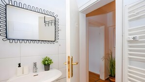 Un baño con un lavamanos blanco, un espejo de marco original, una planta en maceta y una puerta que da a otra habitación.