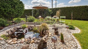 Un jardín con un estanque, rocas, un pabellón y un banco.
