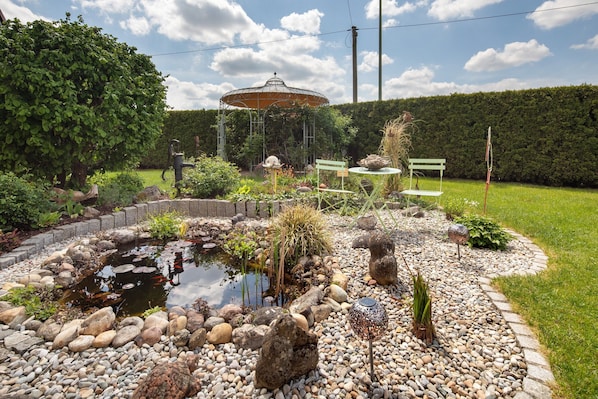 A garden with a pond, rocks, a gazebo, and a bench.