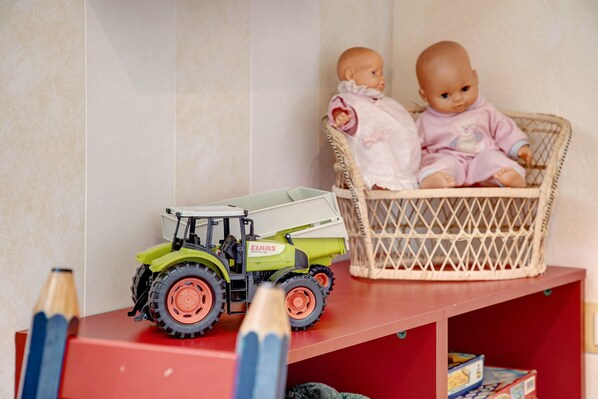A toy tractor, two dolls, and a wicker basket on a shelf.