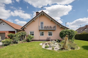 A two-story house with a balcony, a well-maintained lawn, and a small garden area.