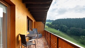 Ein hölzerner Balkon mit Tisch und Stühlen mit Blick auf eine grüne Landschaft.