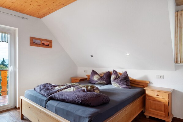 A bedroom with a sloped ceiling, a bed with a blue mattress and purple bedding, wooden nightstands, and a small window with curtains. - Apartment 'St Peter, 55qm' with Shared Garden, Balcony and Wi-Fi (Sankt Peter)