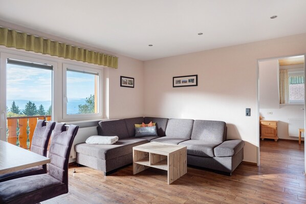 A modern living room with a grey sectional sofa, a wooden coffee table, and a dining table with chairs.