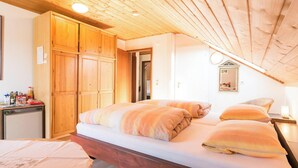 A bedroom with a wooden ceiling, a bed with striped bedding, a wooden wardrobe, and a small desk with a lamp. - Room 'Doppelzimmer Mit Balkon' with Balcony and Wi-Fi (Schömberg)