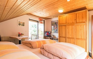 Camera da letto con due letti, soffitto in legno, una scrivania con televisore e una finestra.