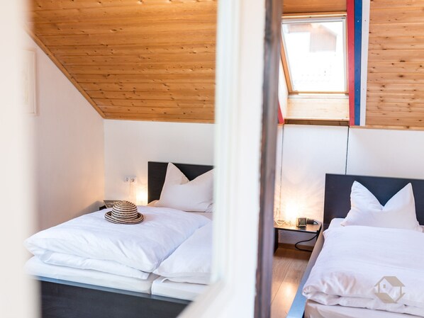 Un dormitorio con dos camas, techo de madera y un tragaluz.