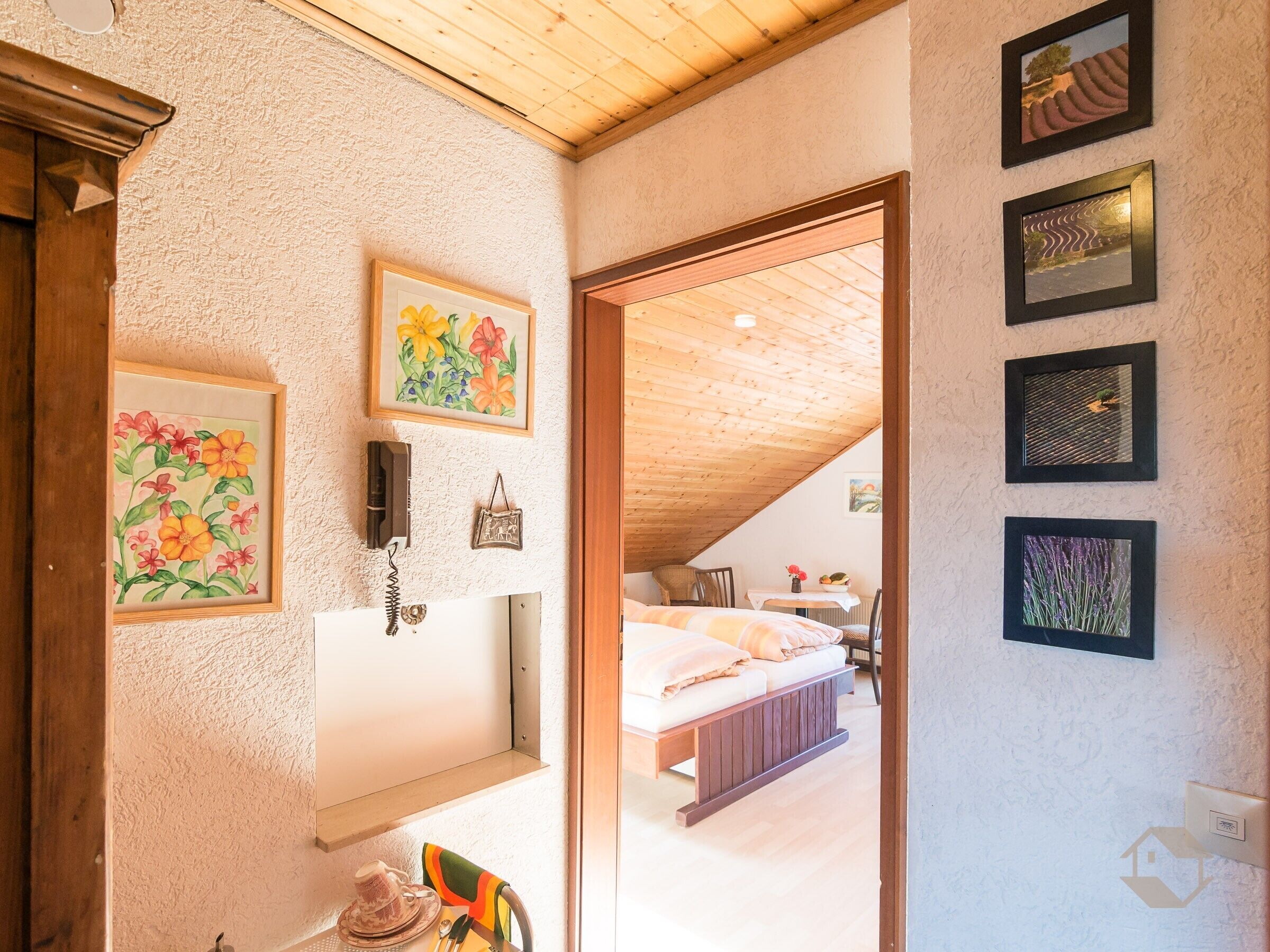 A bedroom with a wooden ceiling, a bed, a bedside table, and a wall-mounted telephone.