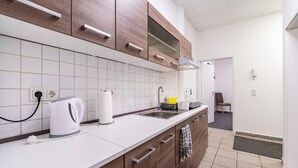 A modern kitchen with wooden cabinets, a white countertop, and a sink. There is a kettle, a toaster, and a towel hanging on the cabinet.