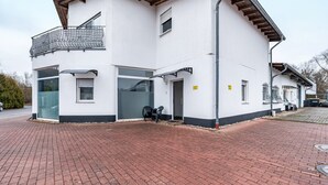A two-story building with a balcony, a garage door, and a paved driveway.